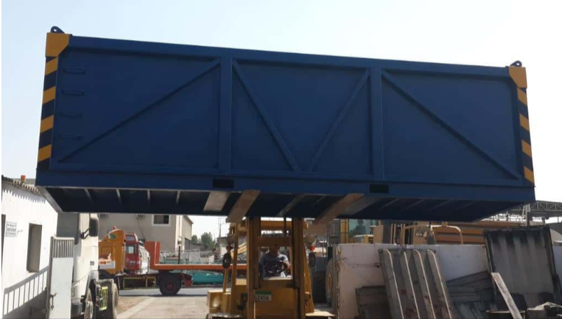 Blue offshore cargo basket being lifted in an industrial yard with reinforced steel structure and safety markings.